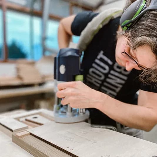 Medewerker van Binthout freest de vorm van een houten borrelplank.