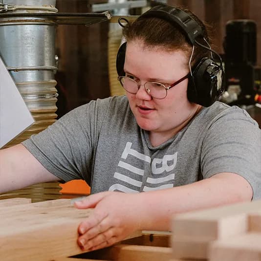 Een medewerker met gehoorbescherming werkt aan hout in de werkplaats van Binthout.