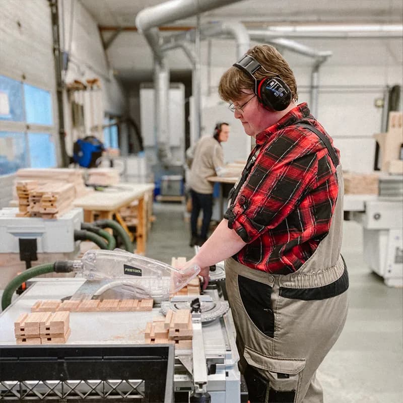 Dezelfde medewerker bij de zaagmachine, met stapels houten onderdelen voor de volgende bestelling.